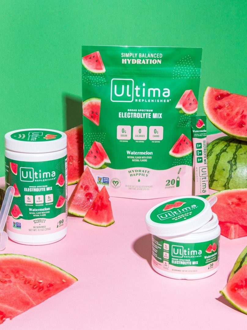 A packet of Ultima Watermelon Electrolyte mix next to a large and small container of the products, with watermelon slices surrounding them.