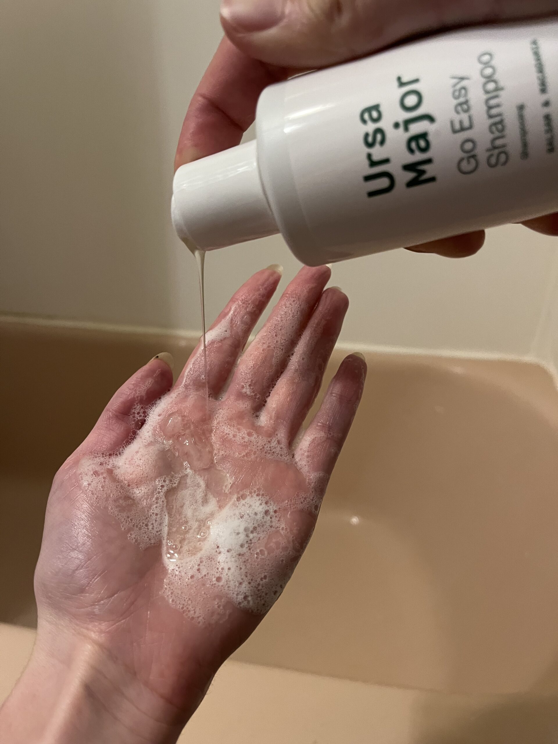 Dispensing shampoo from a bottle onto a palm, creating a foamy lather.