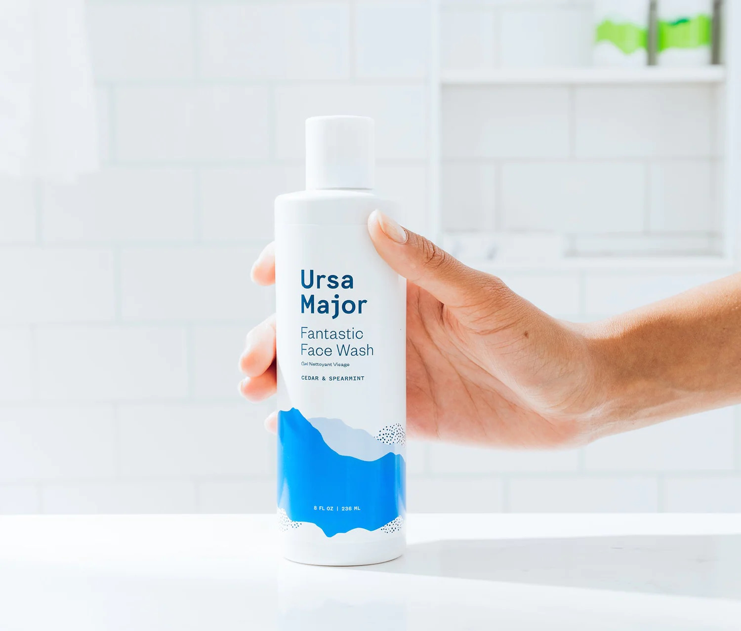 A hand holding a bottle of Ursa Major's Face Wash. 