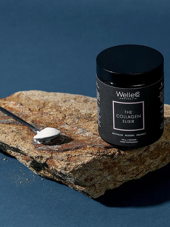 A jar of WelleCo Collagen Elixir on a stone with a spoon of the powder next to it. 