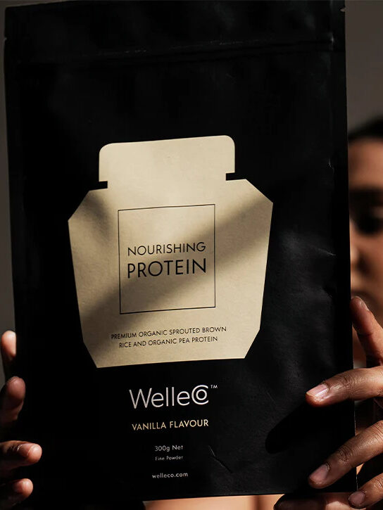 A model in the background holding up a packet of WelleCo Nourishing Protein Powder.