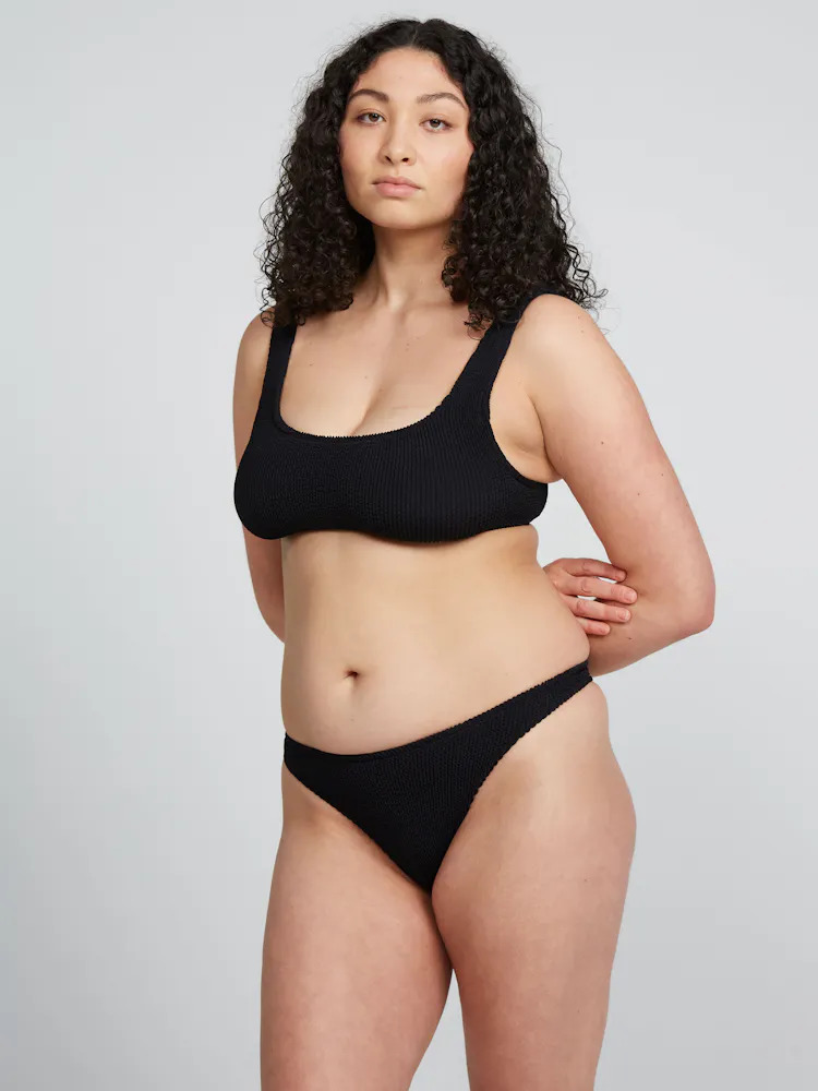 Woman posing in a black bikini set against a neutral background.