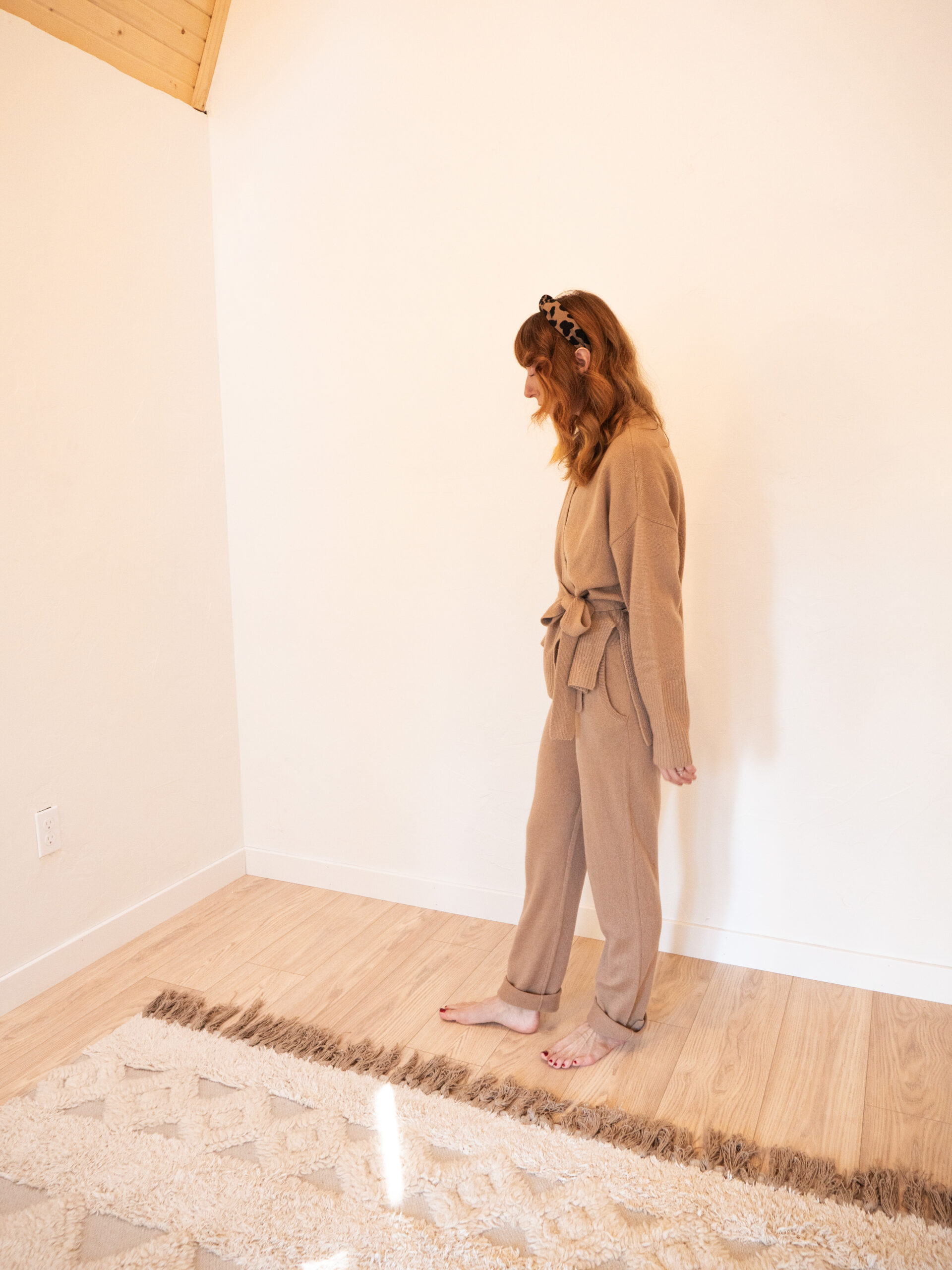 A woman standing in an empty room wearing a tan jumpsuit.
