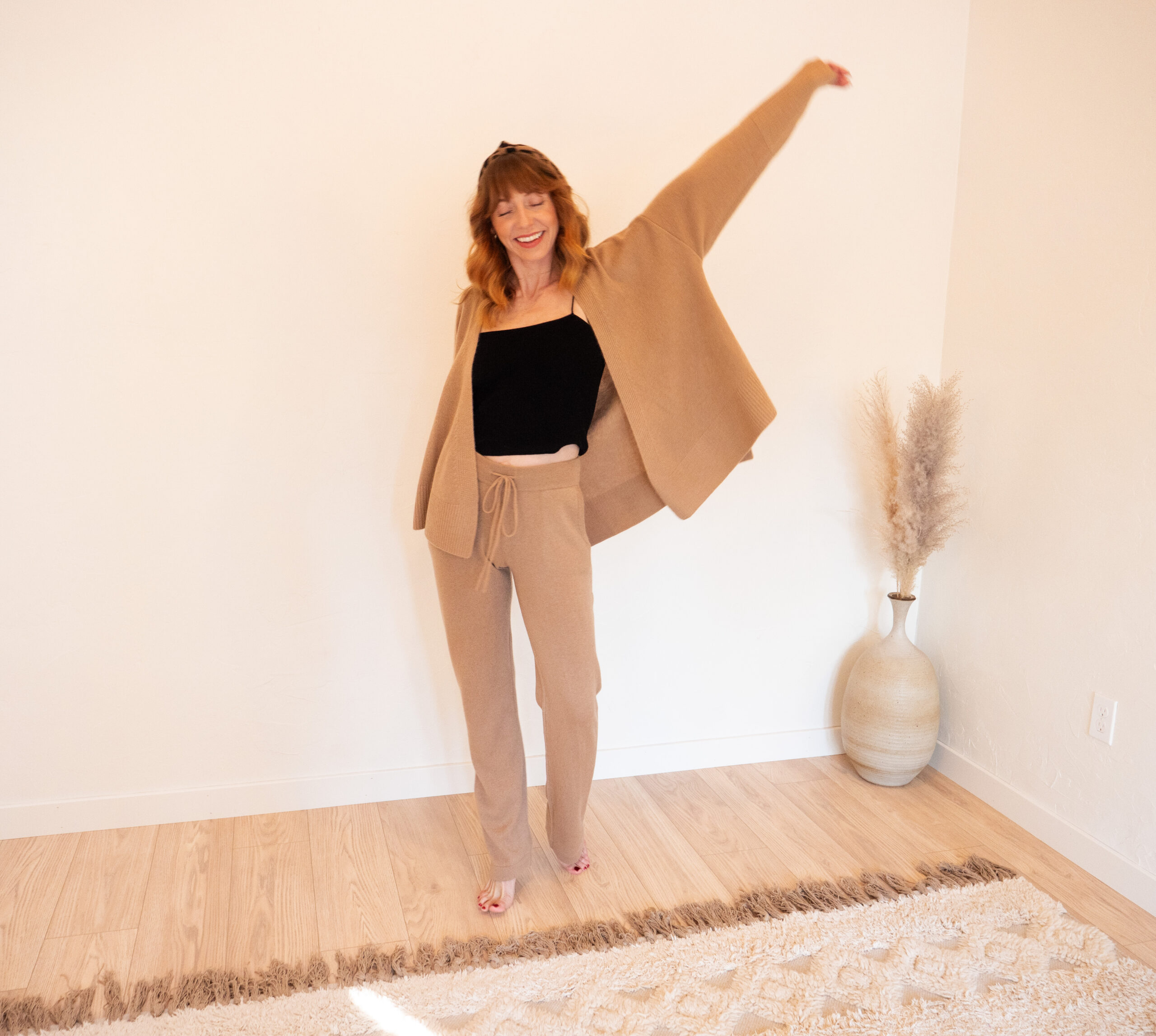 A woman standing in a room wearing a tan sweater and pants.