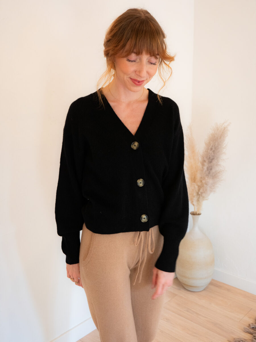 A woman wearing a black cardigan and tan pants.
