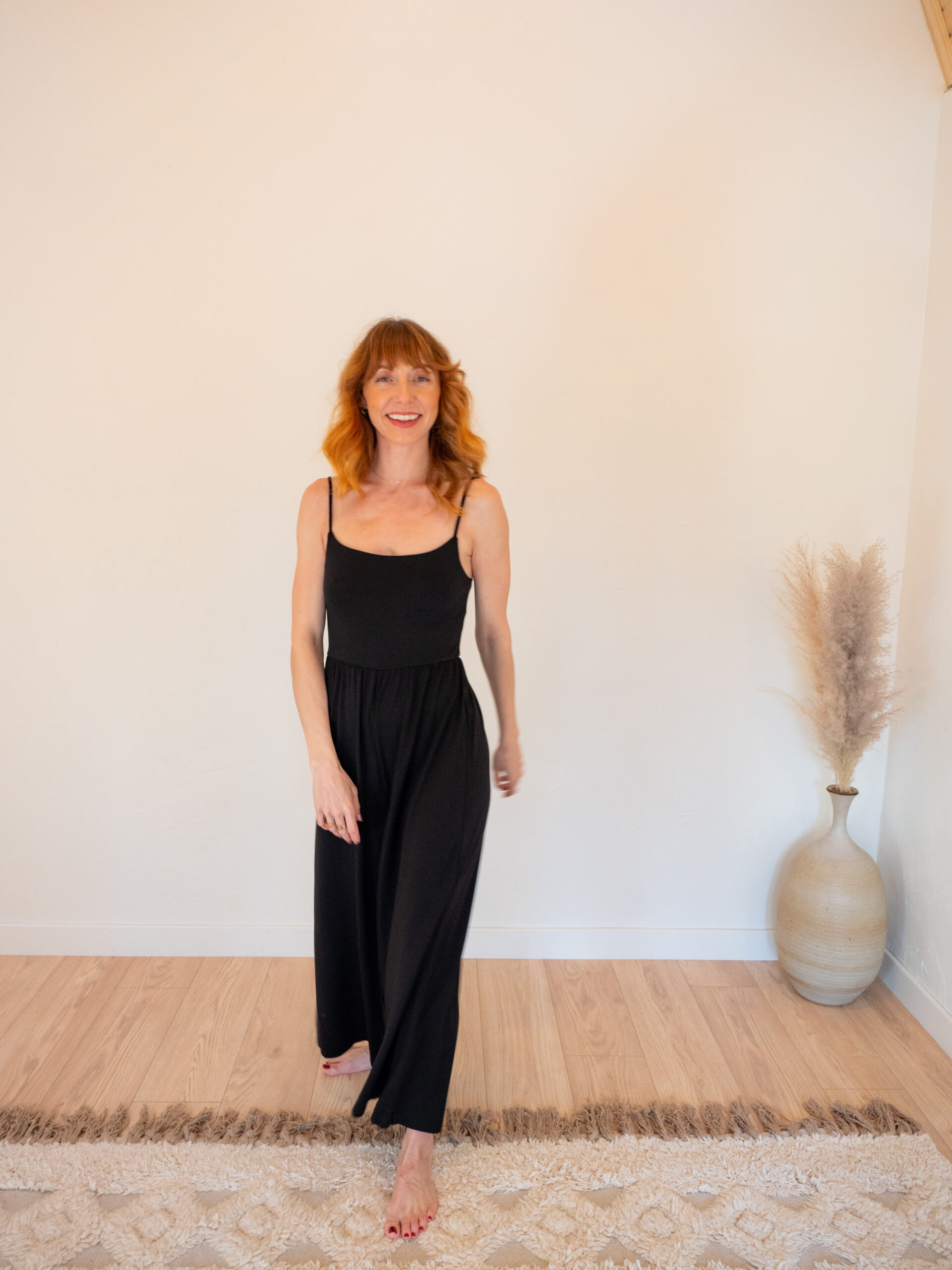 A woman in a black jumpsuit standing on a rug.