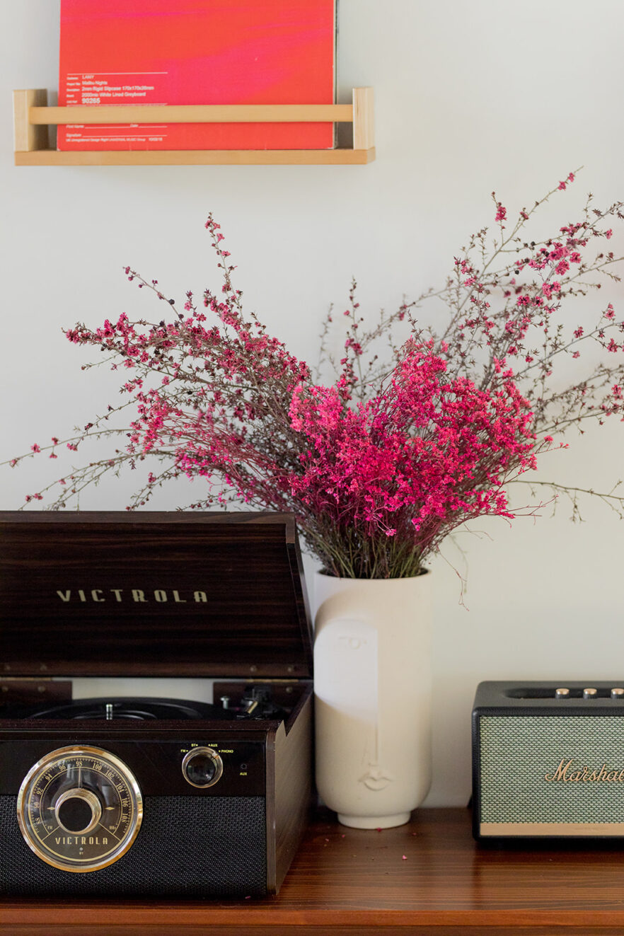 A wooden table with a record player and a vase of flowers.
