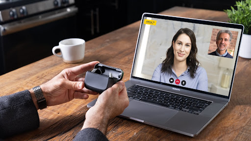 A person connecting a webcam to a laptop displaying a video call with two people.