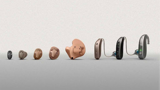 A range of hearing aids in various sizes and designs displayed in size order.