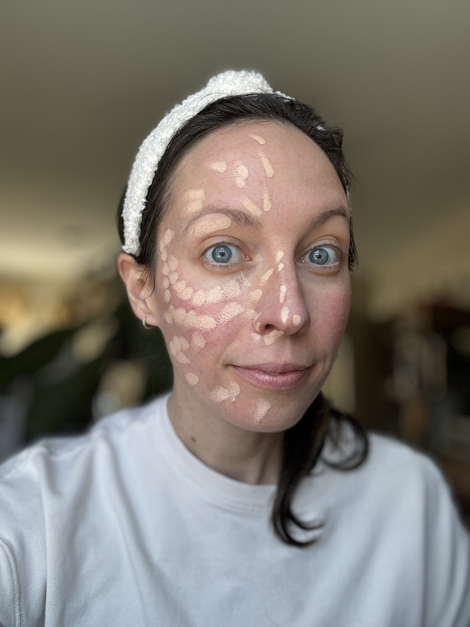 A person with a headband applying foundation makeup on their face.