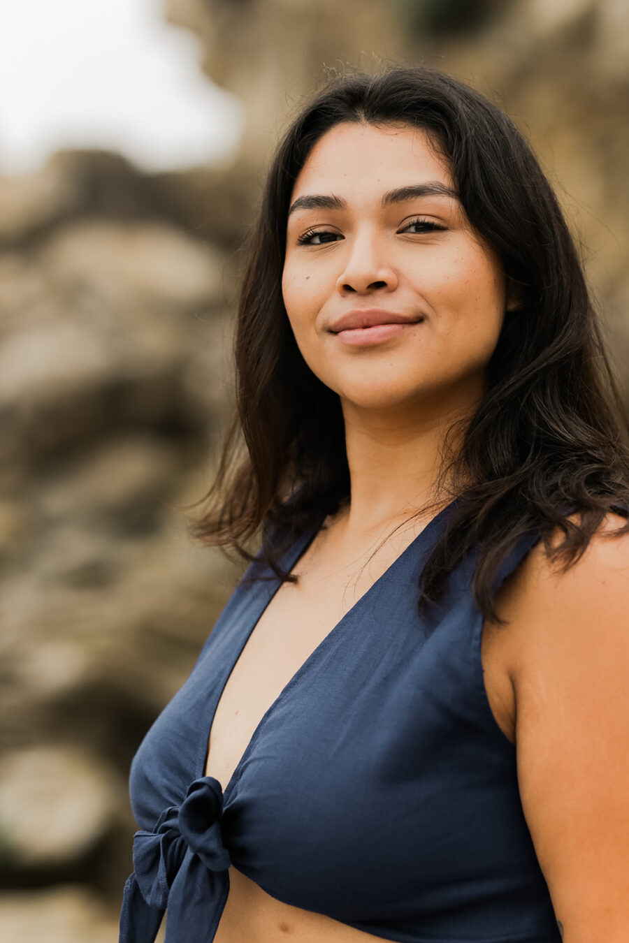 A woman with shoulder-length hair smiling gently at the camera, wearing a blue top, with a blurred natural backdrop.