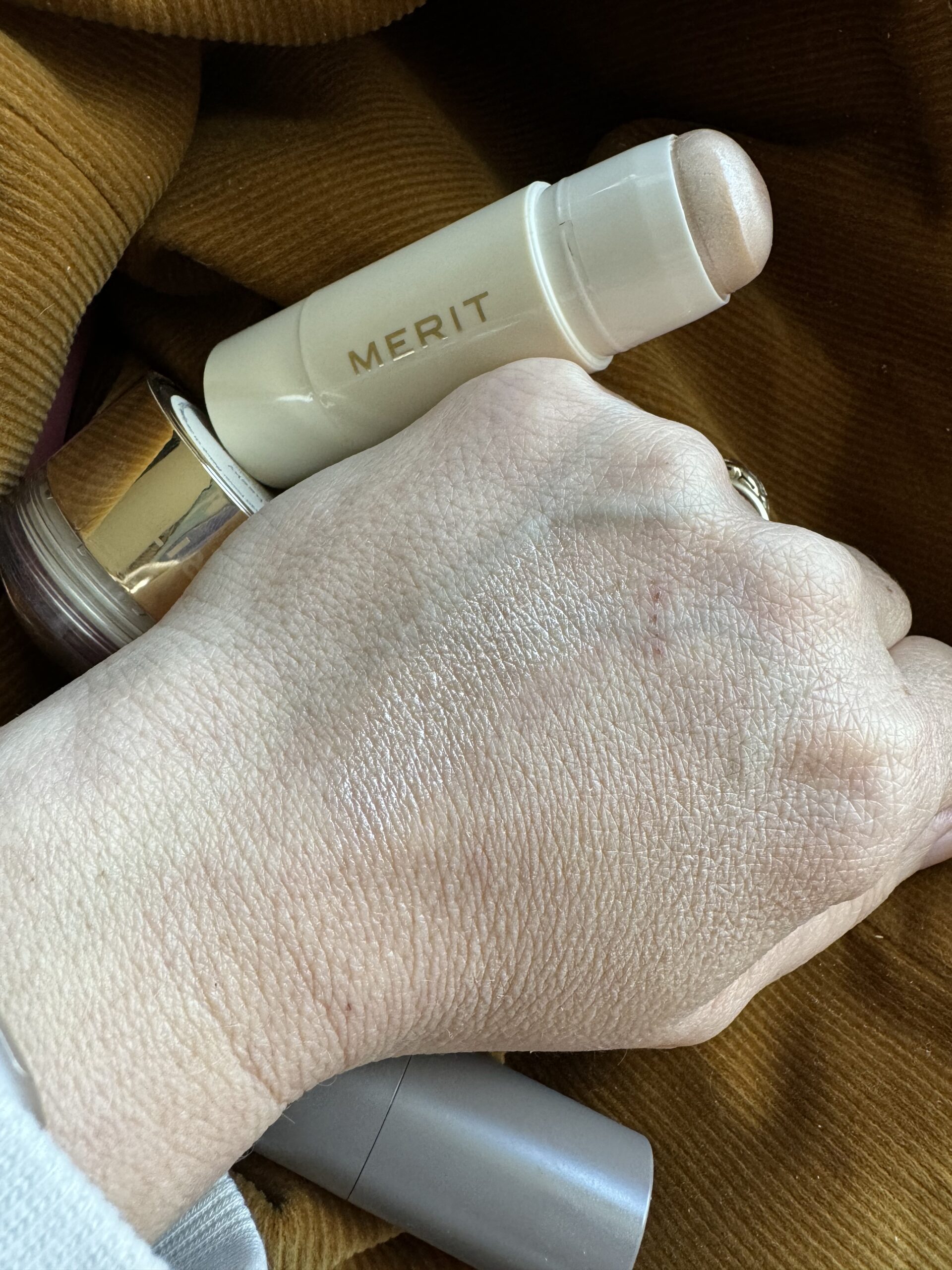 Swatch of cosmetic product on the back of a hand with cosmetic packaging in the background.