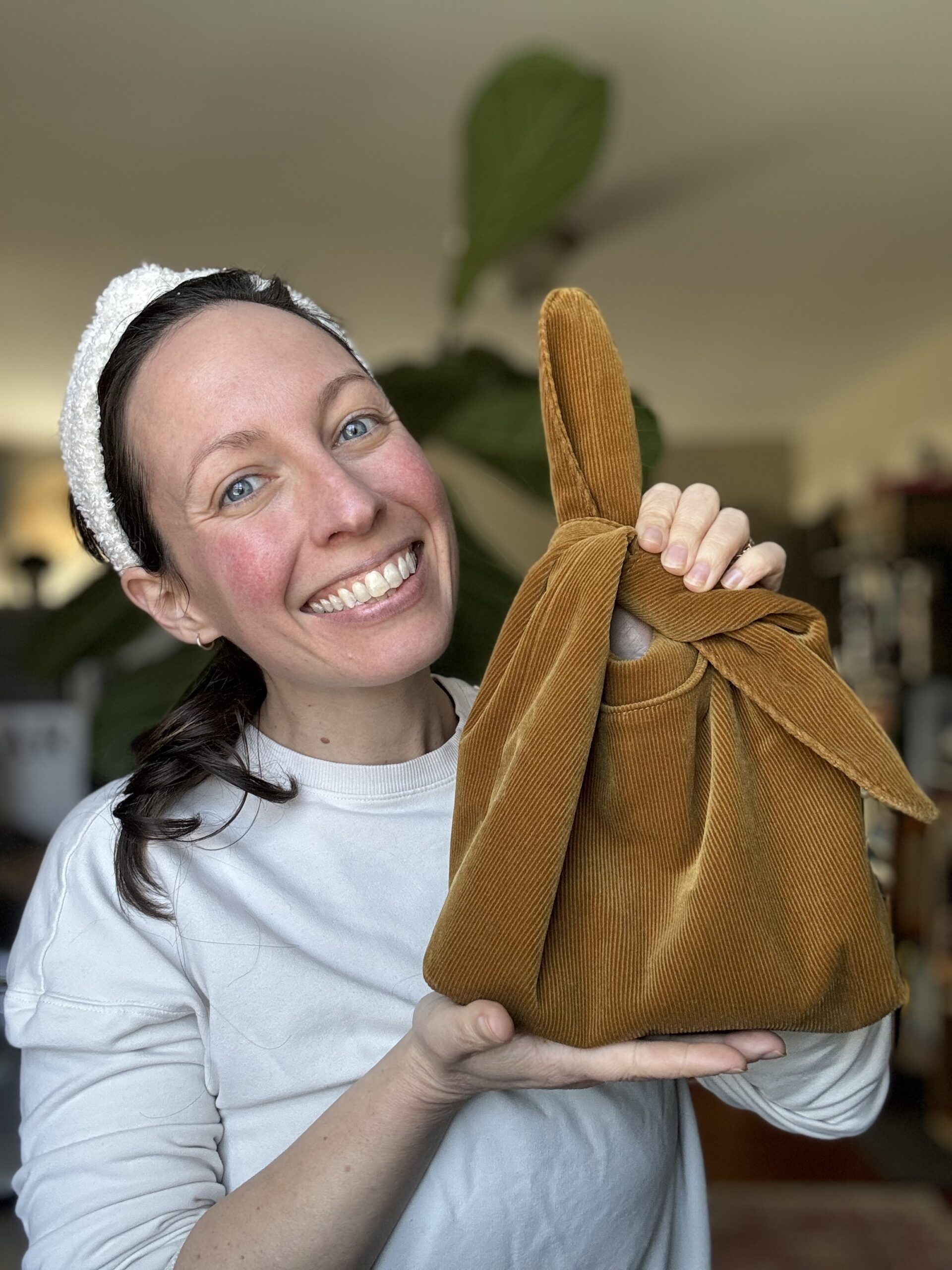 A smiling woman holding up a brown fabric bag with a knot.