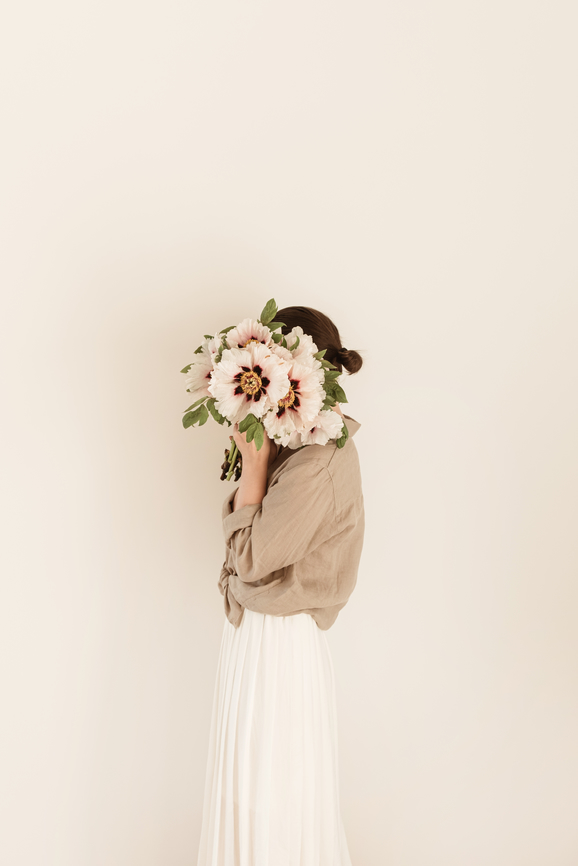 Young pretty woman with peonies bouquet standing against neutral beige wall