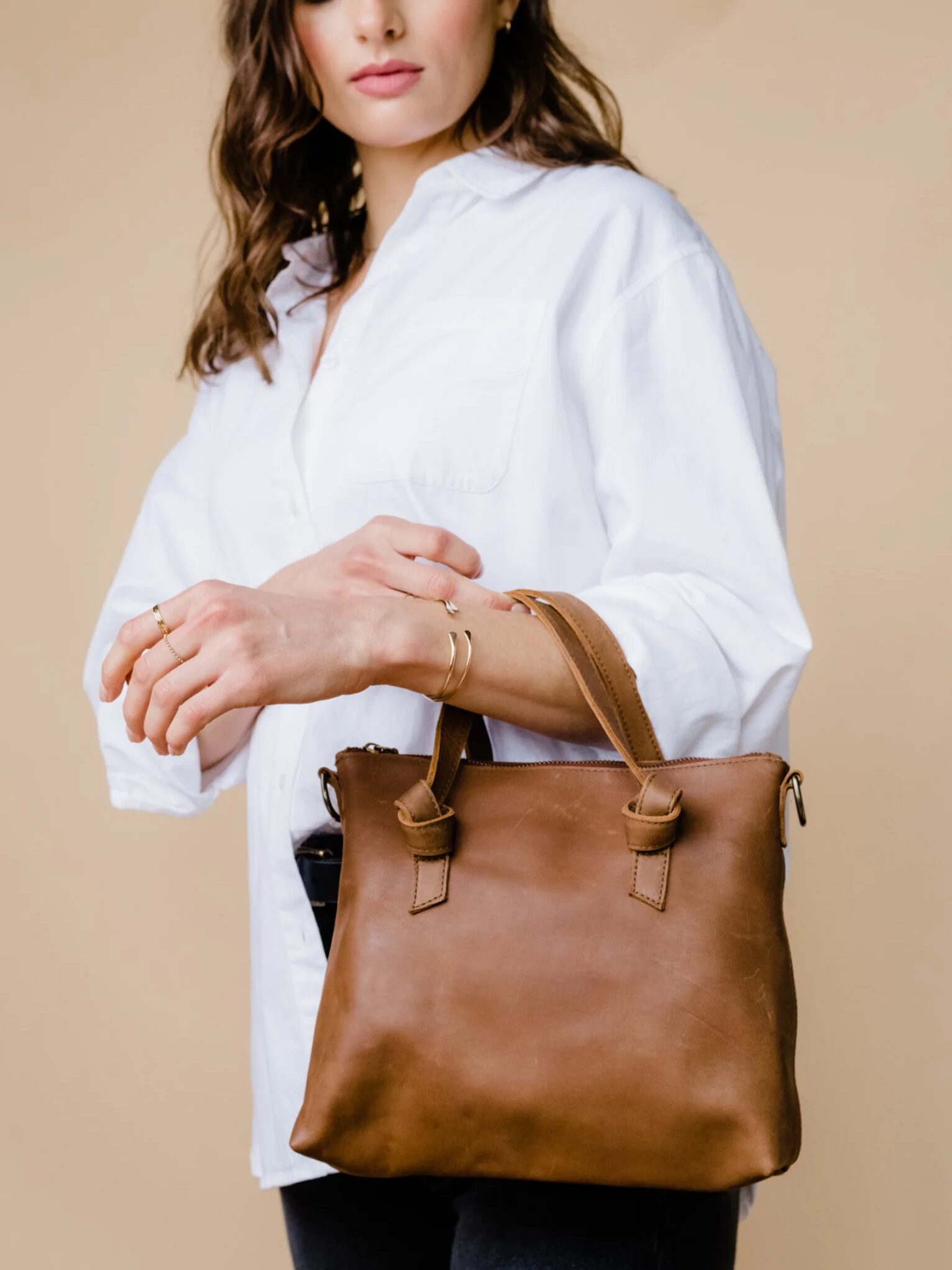 Woman holding a brown leather bag while wearing a white blouse.
