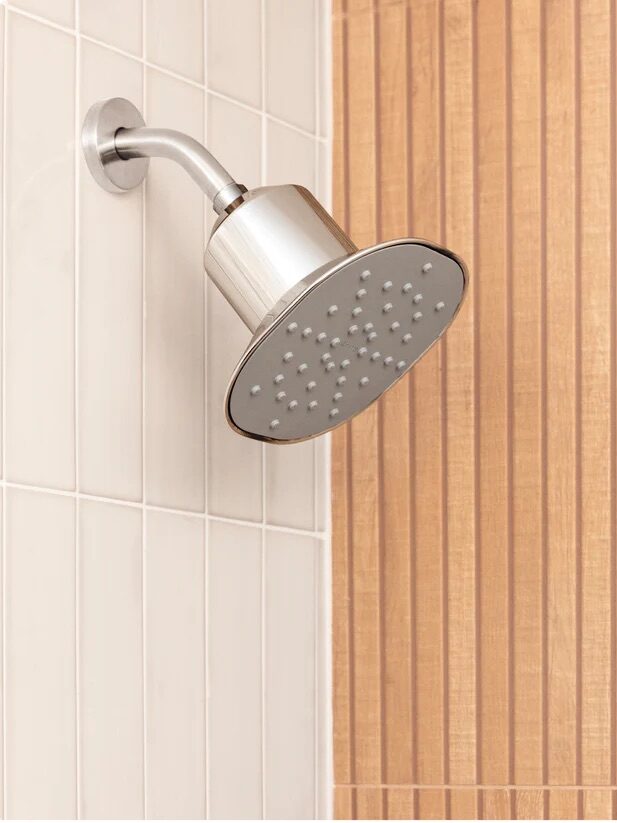 Stainless steel showerhead against a tiled wall.