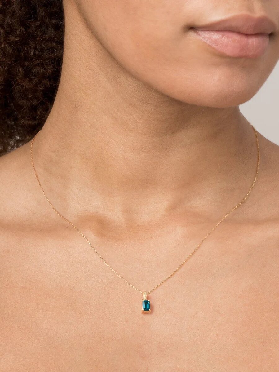 Woman wearing a gold necklace with a blue rectangular pendant.