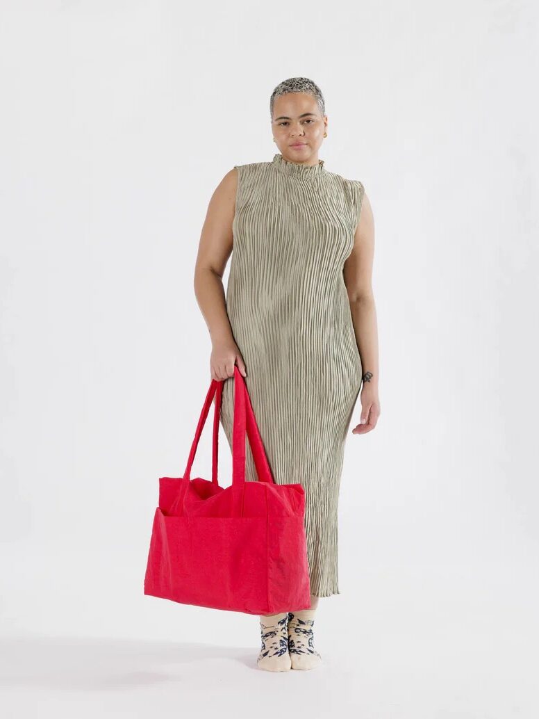 A person in a striped dress holding a red tote bag stands against a white background.