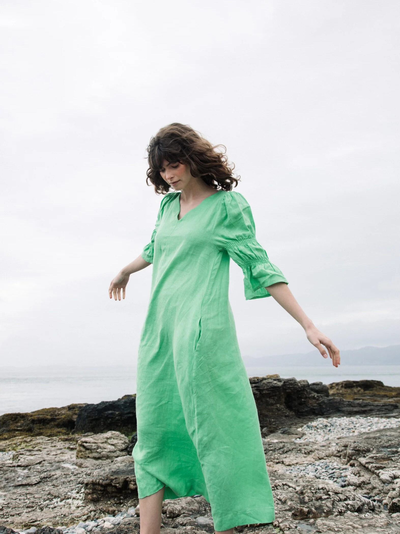 A woman in a green dress standing on a rocky beach.