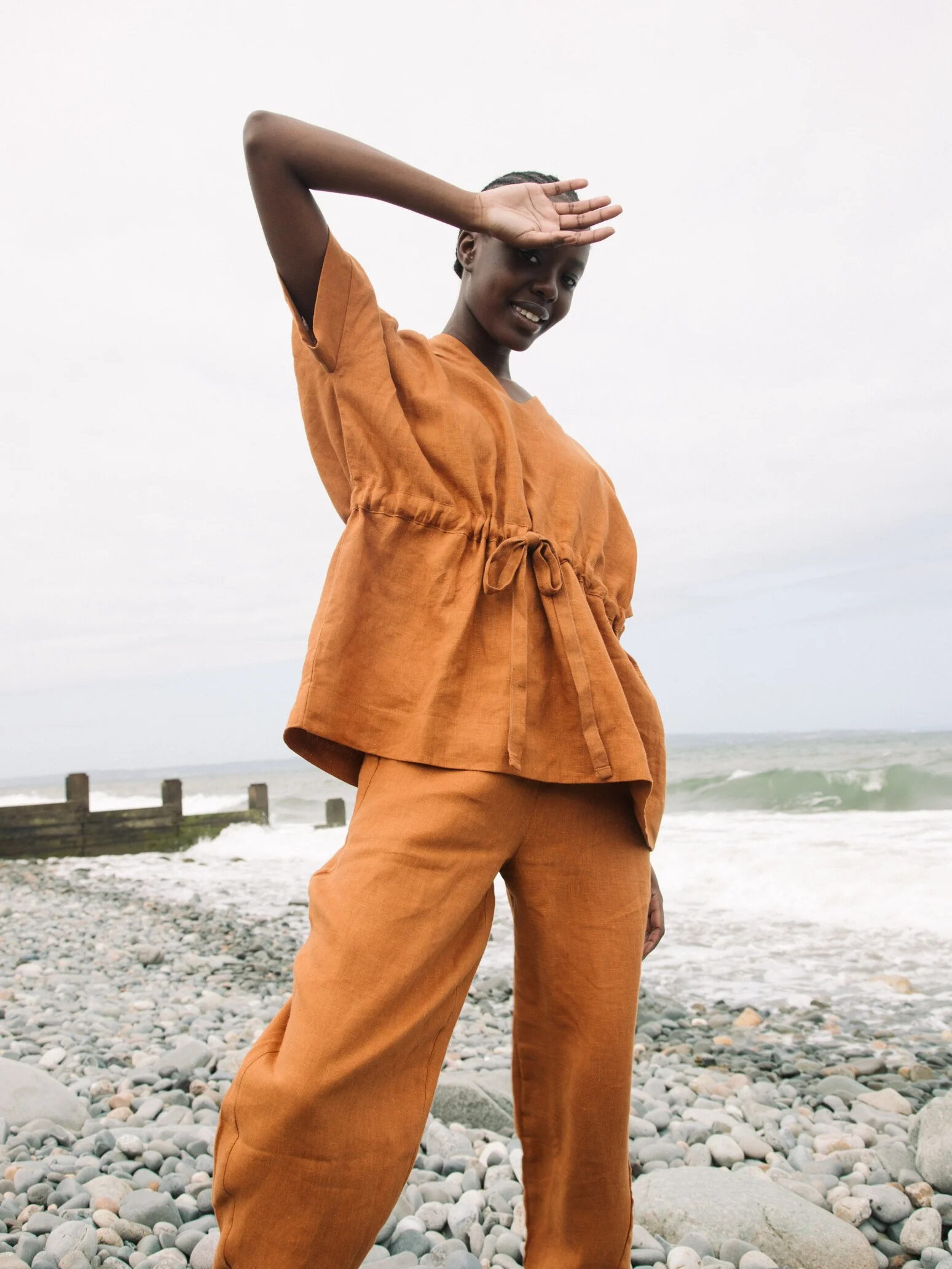 A woman in an orange jumpsuit standing on a beach.