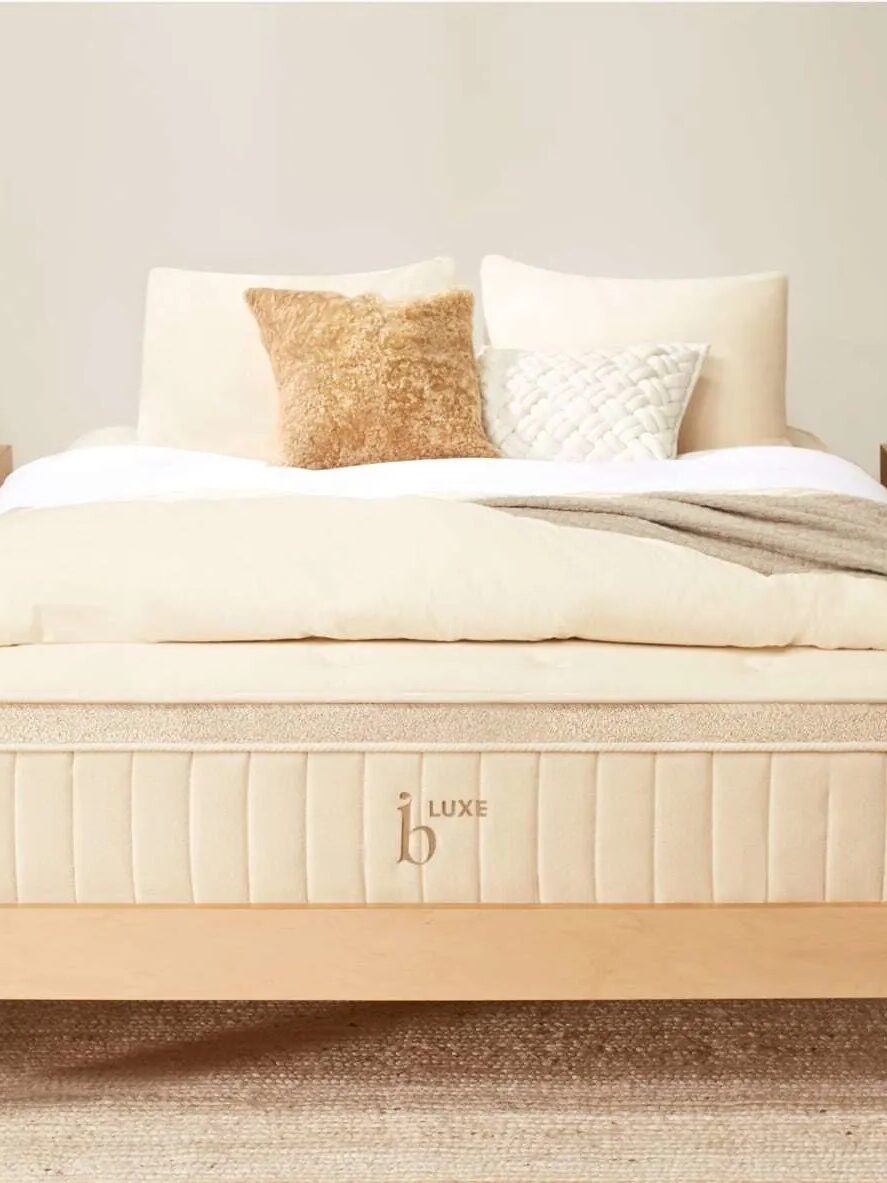 A neatly made bed with a wooden frame, white and beige bedding, and two side tables with lamps.