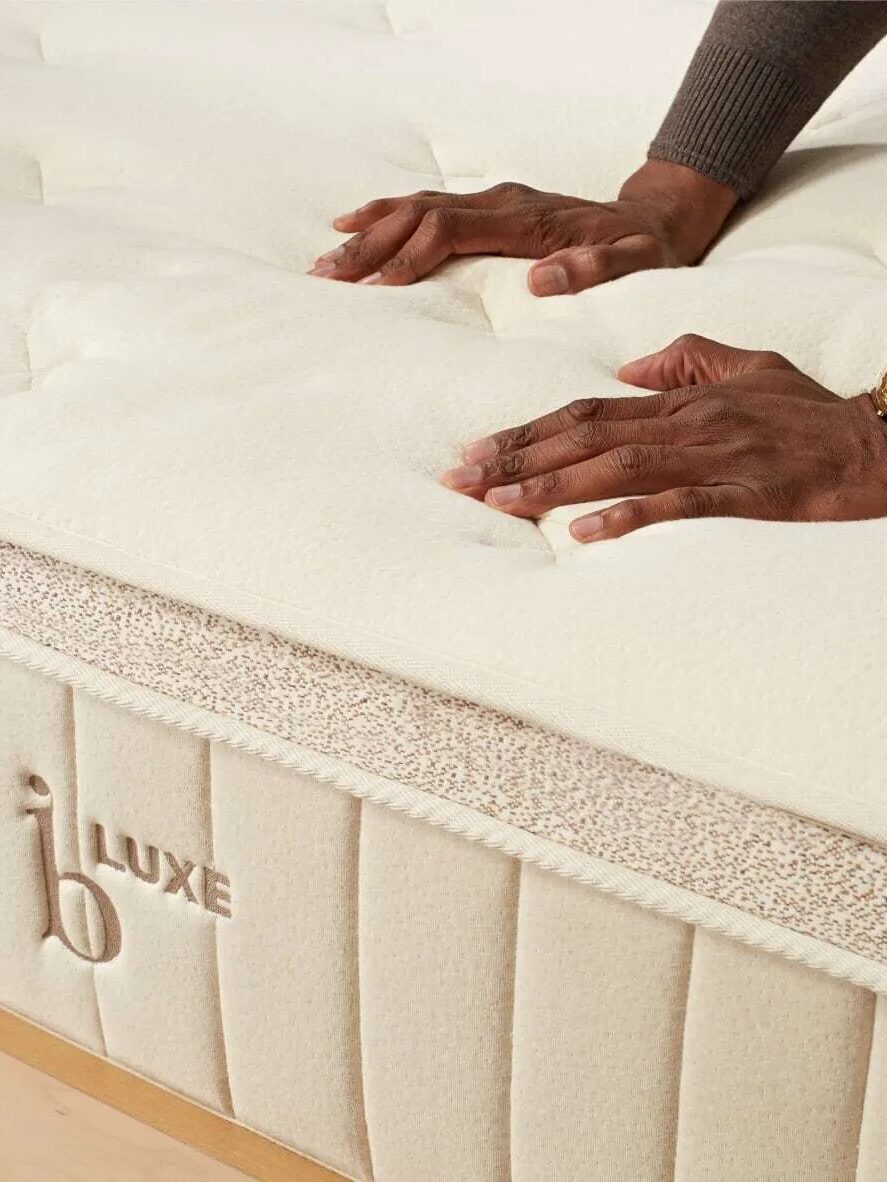 Person pressing down on a plush mattress to check its firmness.