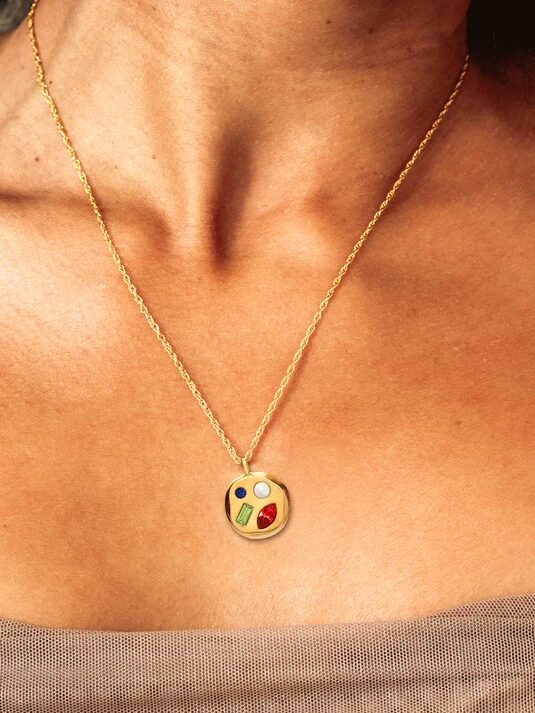 A gold pendant necklace with an abstract design worn by a person.