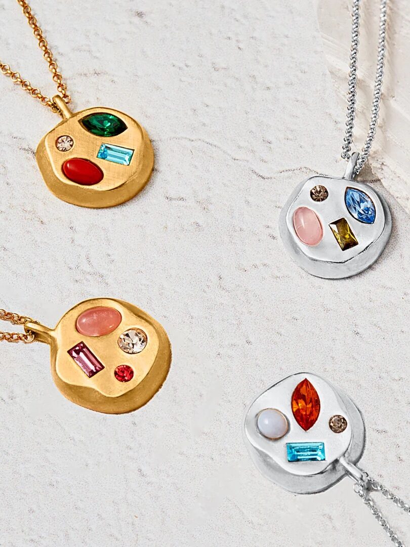 Four gemstone-embellished pendants on a marble surface.