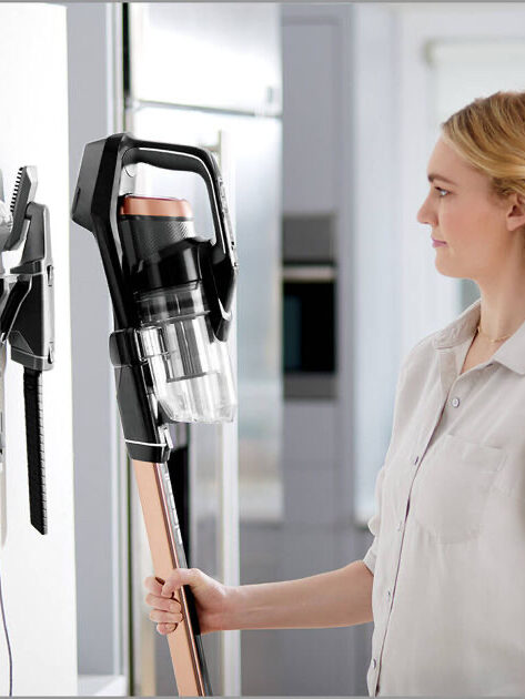 Woman examining a cordless vacuum cleaner mounted on a wall docking station.