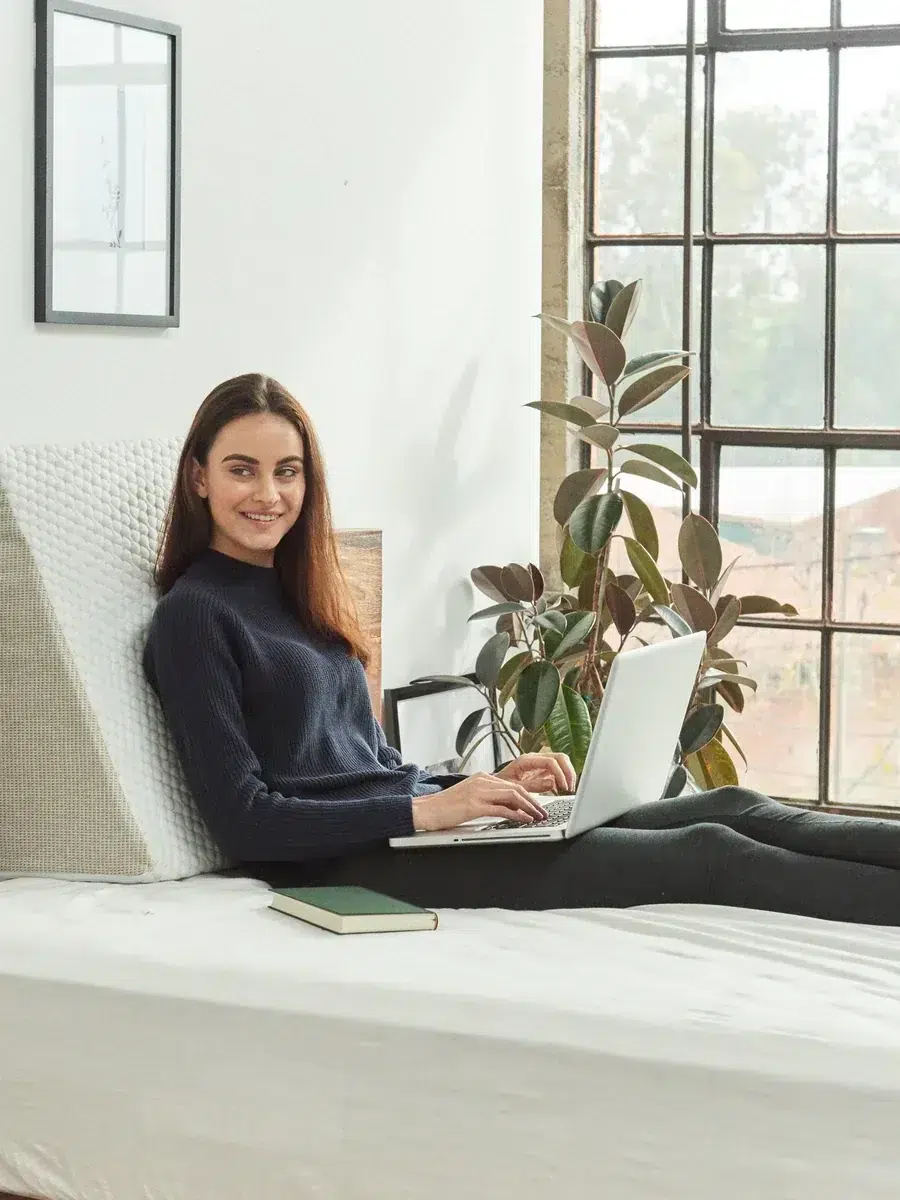 A woman sitting on a bed with a laptop in her lap.