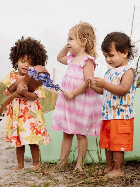 A group of children are standing on a beach with a guitar.