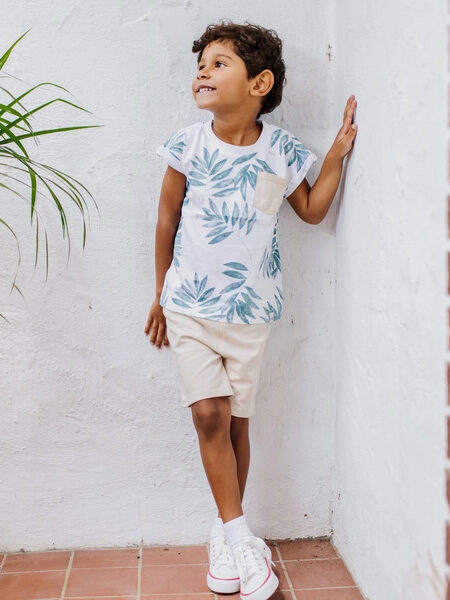 A young boy wearing a t - shirt and sneakers leaning against a wall.