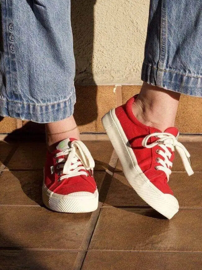 Person wearing red sneakers with white laces standing on a tiled floor.