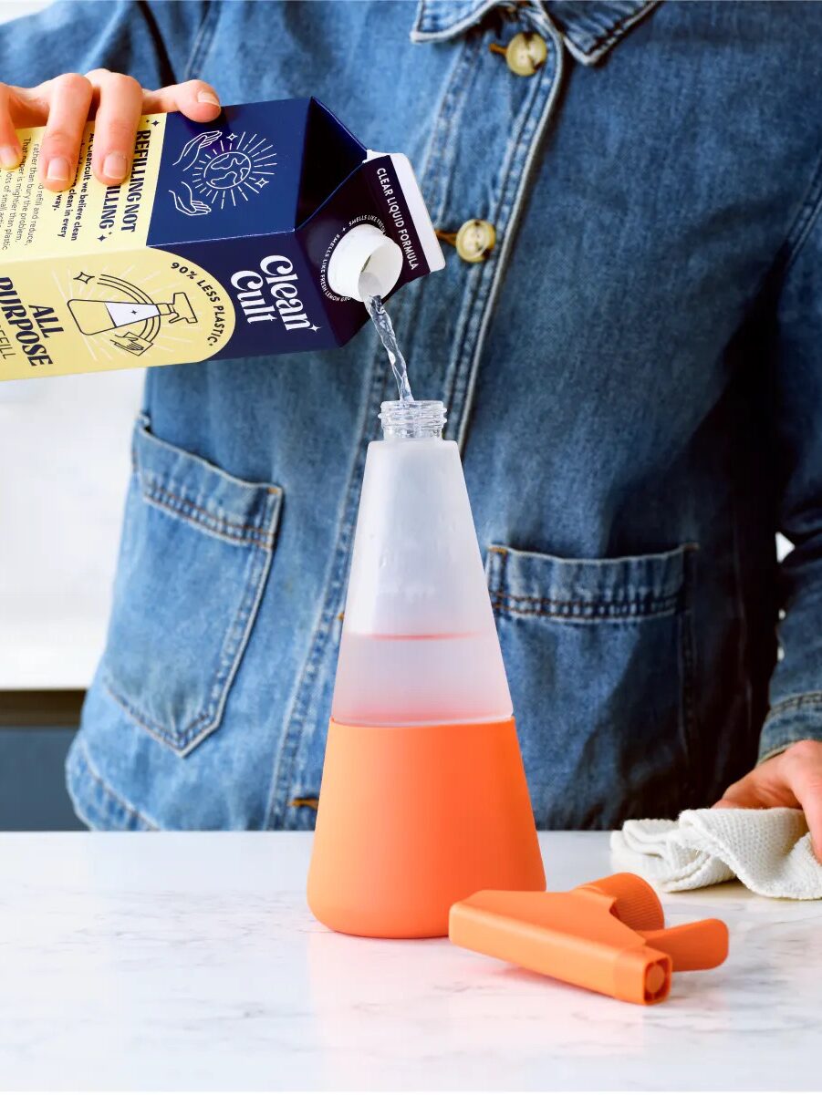 A person pouring cleaning solution into a spray bottle on a kitchen counter.