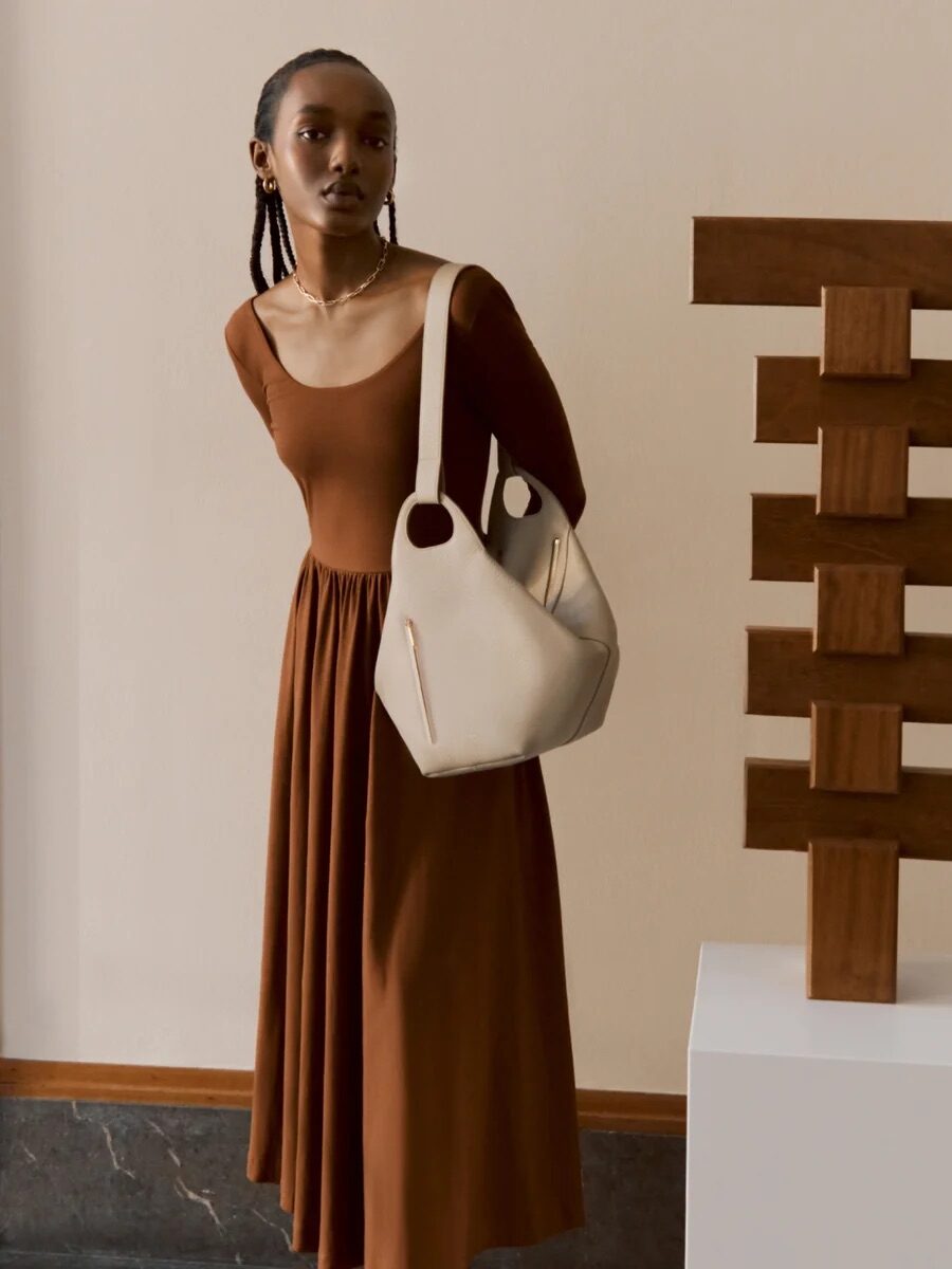 Two women posing with handbags next to a sculpture and a window.