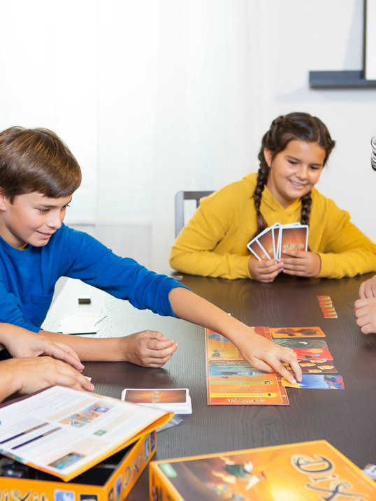 Group of children engaged in a board game, smiling and focused on the cards.