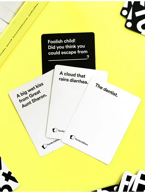 A photo of playing cards from a humorous fill-in-the-blank card game displayed on a yellow background.