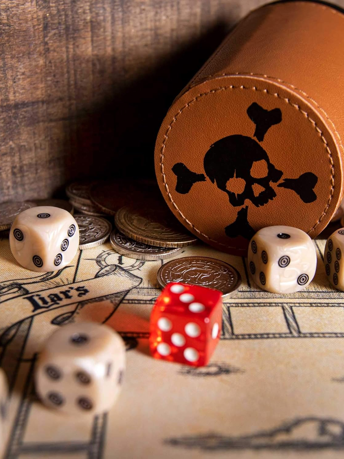 Dice, coins, and a leather cup with a skull-and-crossbones symbol on a table, suggesting elements of a pirate-themed game.