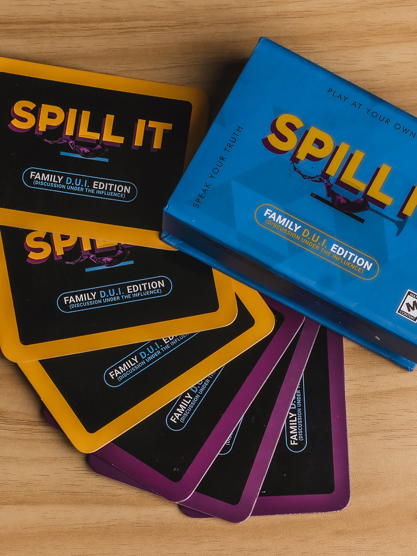 A "spill it" board game box with its family edition cards spread out on a wooden surface.