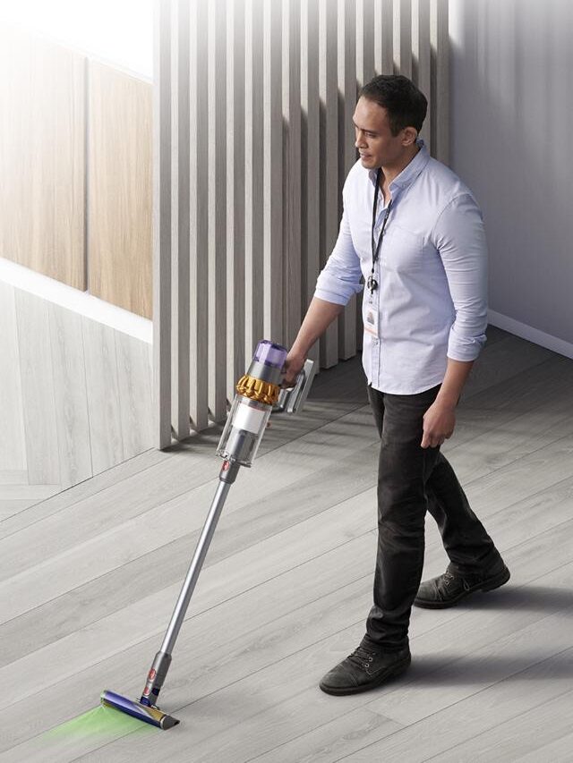 Man using a cordless vacuum cleaner on a hardwood floor.