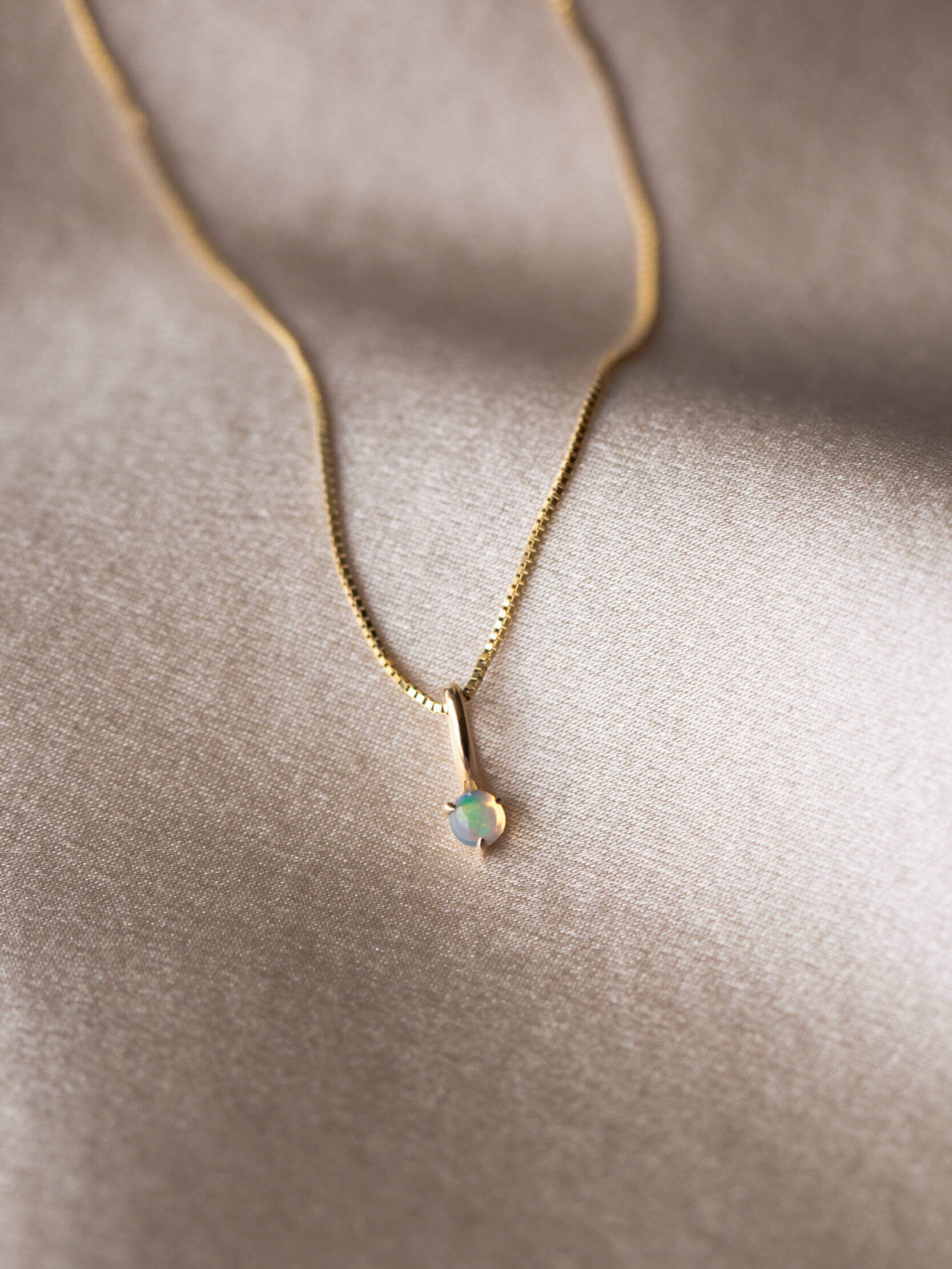 Gold necklace with a single gemstone pendant on a beige fabric surface.