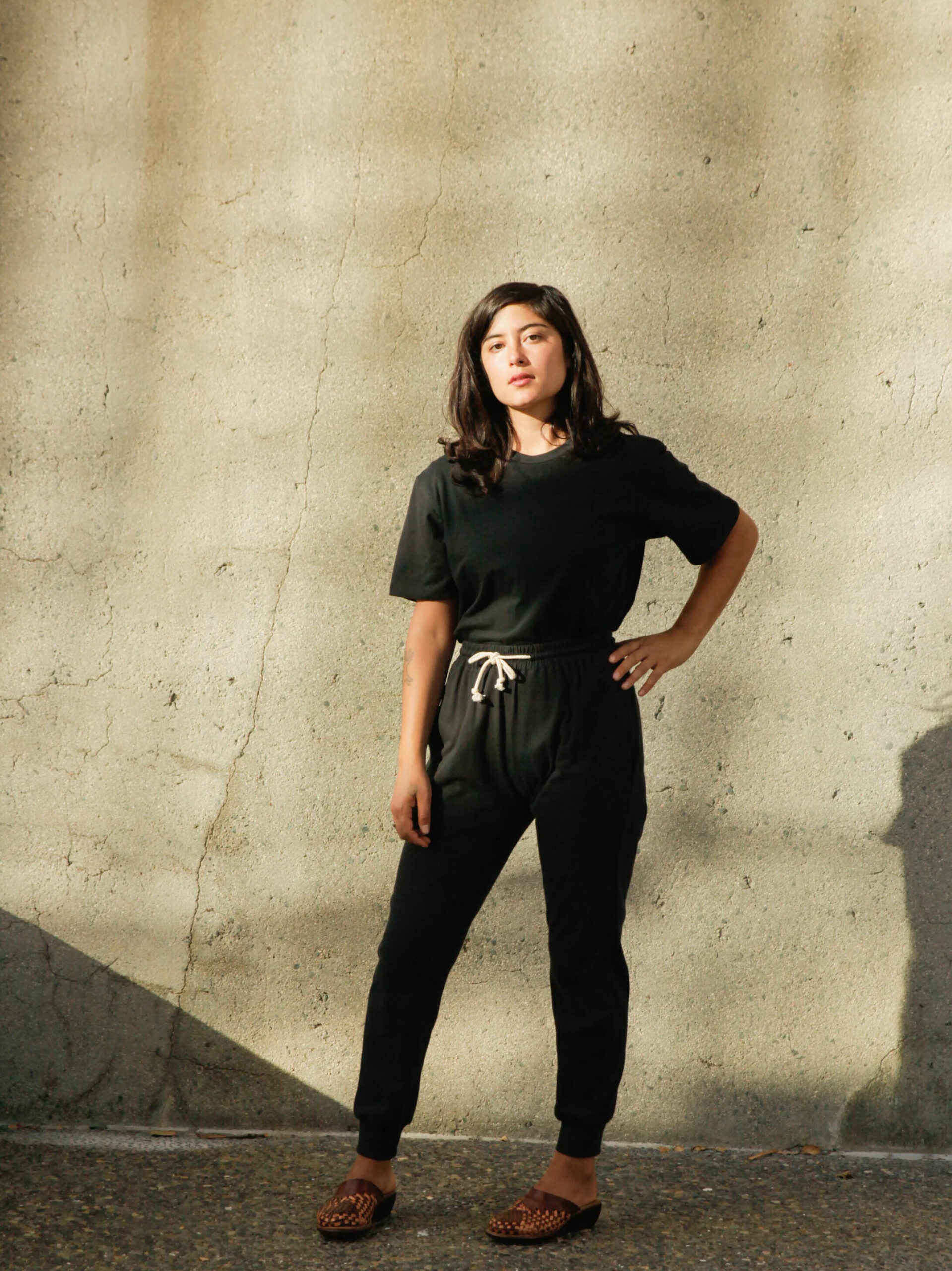 A woman in black standing next to a concrete wall.