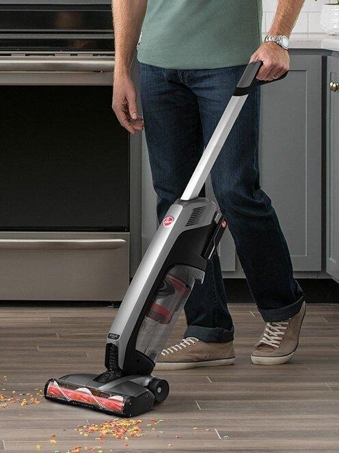 A person using a cordless stick vacuum cleaner to clean up a spill on a kitchen floor.
