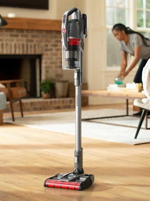 A person cleans the floor with a cordless vacuum cleaner in a well-lit living room.