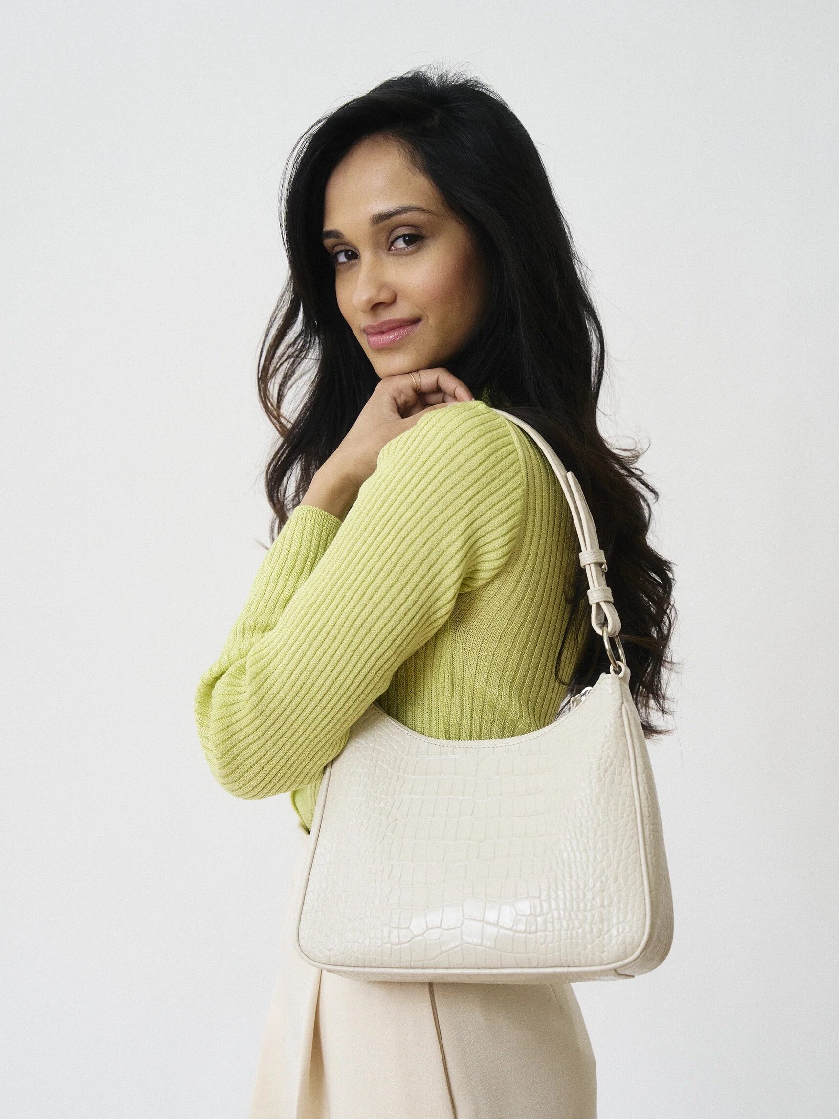 Woman with shoulder bag posing in a yellow sweater and beige pants.