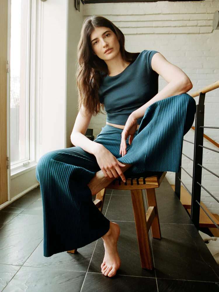 A woman sitting on a chair in a blue top and wide leg pants.