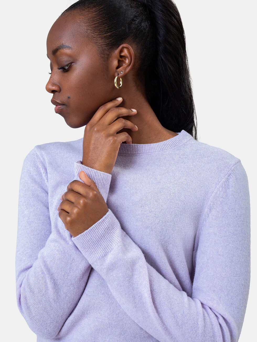 A woman in a lavender sweater gazes to the side with her hand on her neck.