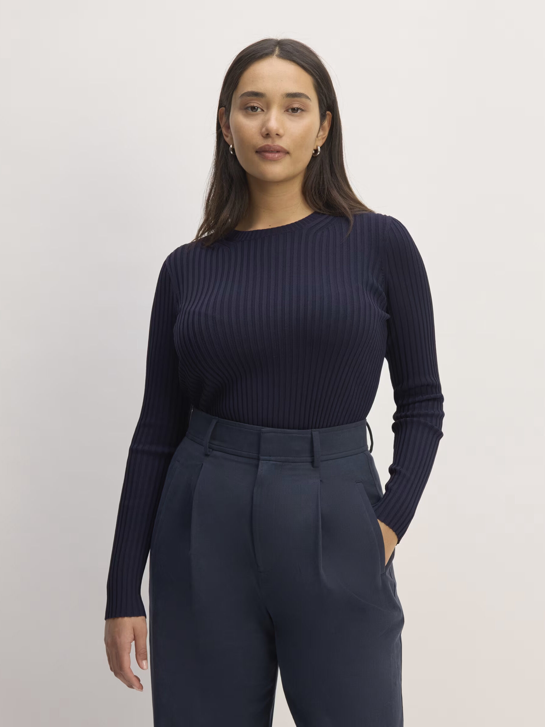 Woman in a navy blue ribbed top and trousers standing against a white background.