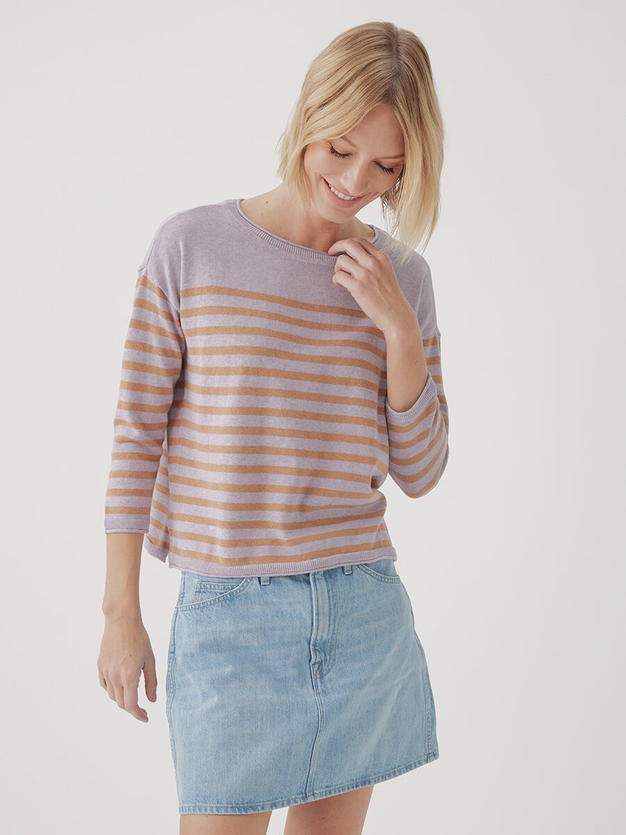 Woman wearing a striped shirt and denim skirt smiling down to her side.