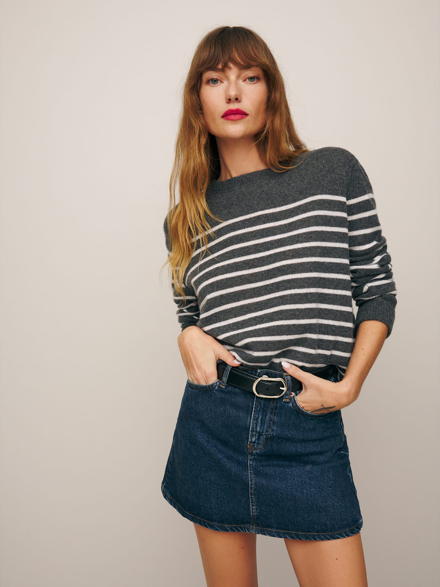 Woman in a striped sweater and denim skirt posing with one hand on her hip.